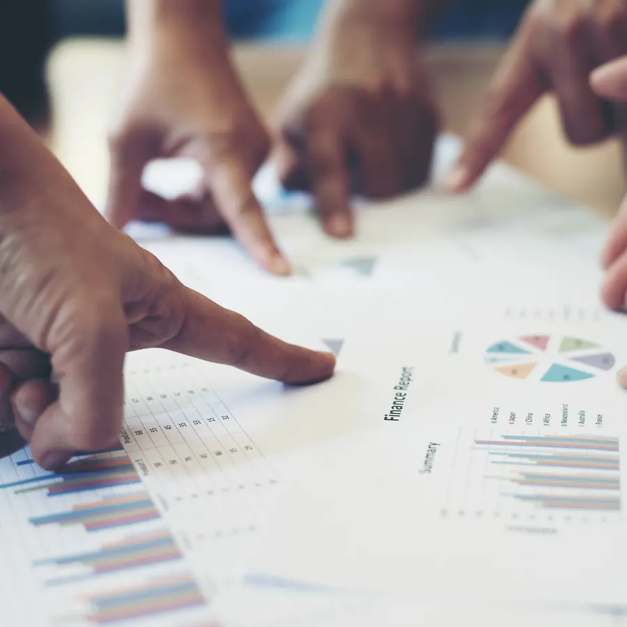 Plusieurs mains désignent ensemble les graphiques d'un rapport financier posé sur une table : l'examen collégial d'une décision.